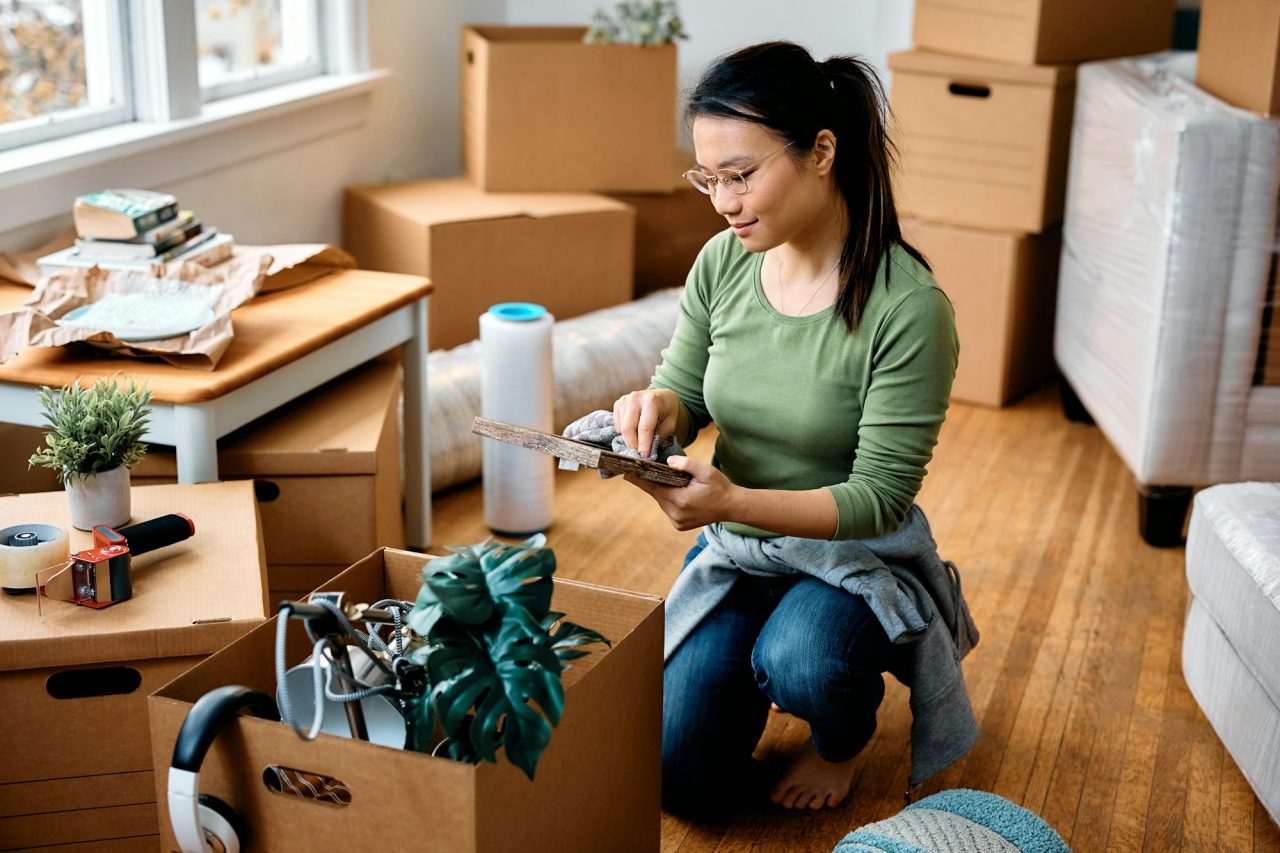 Young  woman cleaning photo frame while unpacking her belongings and moving in a new home.