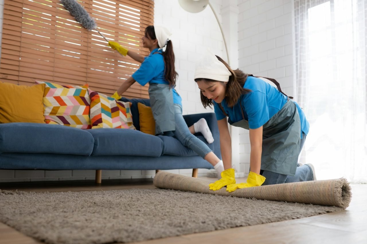 Young women cleaning maid in uniform and rubber gloves are cleaning the room, fold up carpet